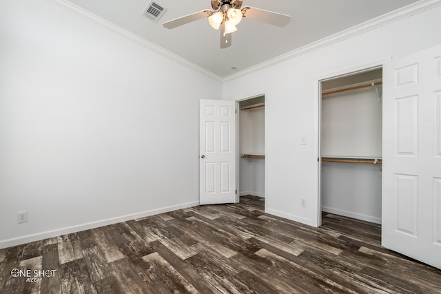 unfurnished bedroom featuring crown molding, dark wood-type flooring, ceiling fan, and two closets