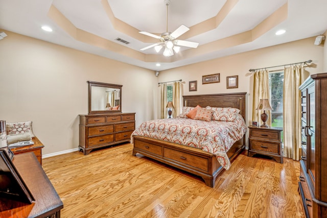 bedroom featuring multiple windows, ceiling fan, a tray ceiling, and light hardwood / wood-style flooring