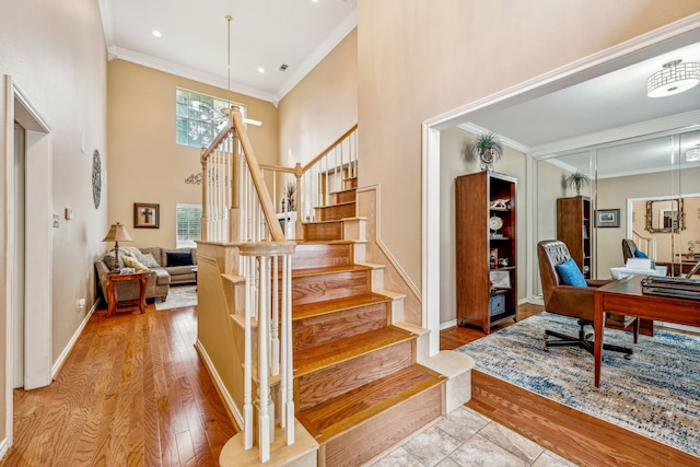 stairs with a high ceiling, hardwood / wood-style flooring, and crown molding