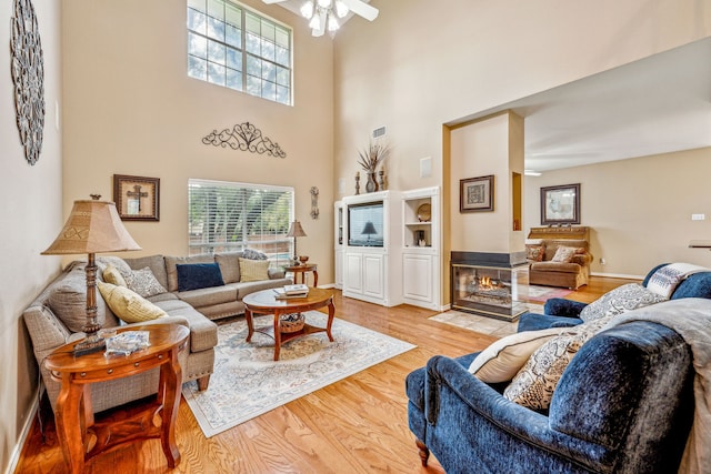 living room featuring ceiling fan, a towering ceiling, and light hardwood / wood-style floors