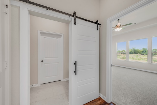 interior space featuring a barn door, ceiling fan, and light colored carpet