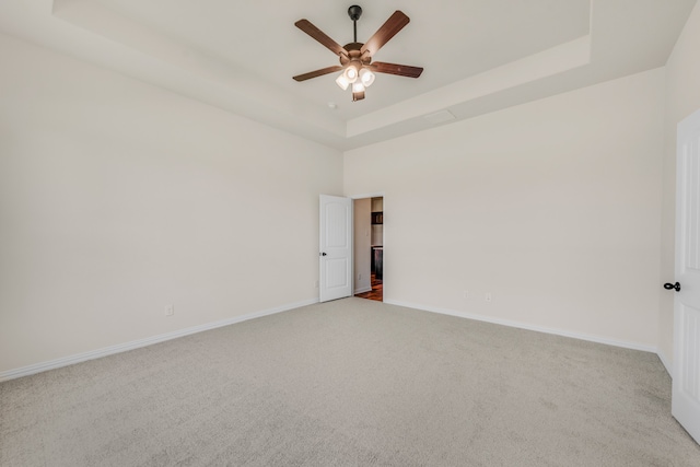 carpeted spare room featuring a tray ceiling and ceiling fan