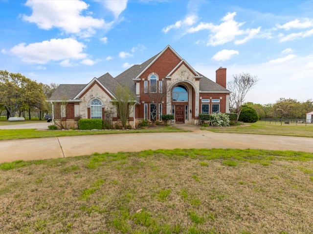 traditional home with stone siding, a chimney, curved driveway, a front lawn, and brick siding