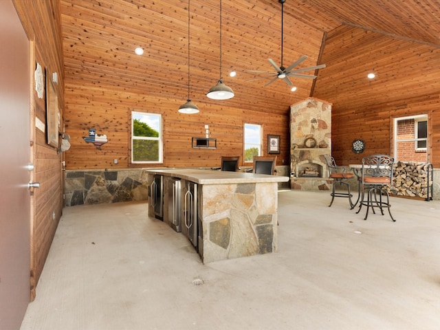 interior space featuring hanging light fixtures, ceiling fan, wood walls, high vaulted ceiling, and a center island with sink