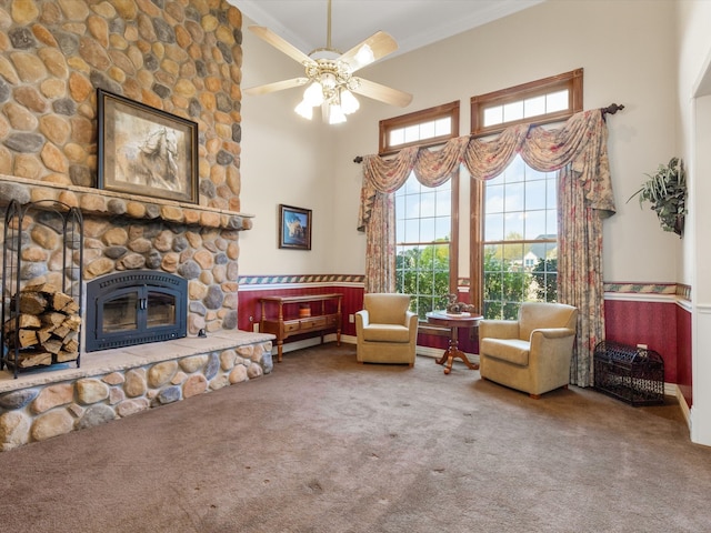 living room featuring a high ceiling, ornamental molding, ceiling fan, a stone fireplace, and carpet floors