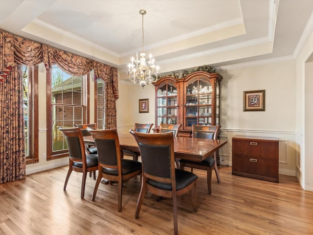 dining space featuring a raised ceiling, a notable chandelier, crown molding, and light wood finished floors