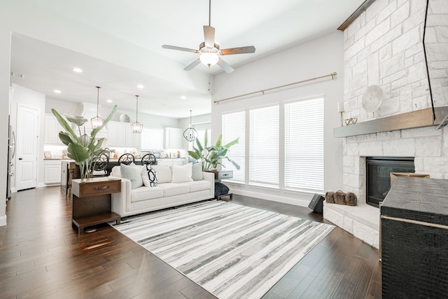 living room with ceiling fan with notable chandelier, a fireplace, and dark hardwood / wood-style floors