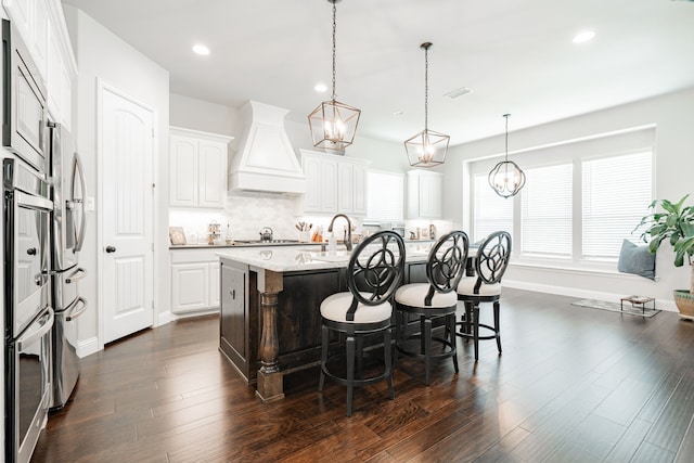 kitchen featuring custom exhaust hood, white cabinetry, stainless steel appliances, an island with sink, and dark hardwood / wood-style floors