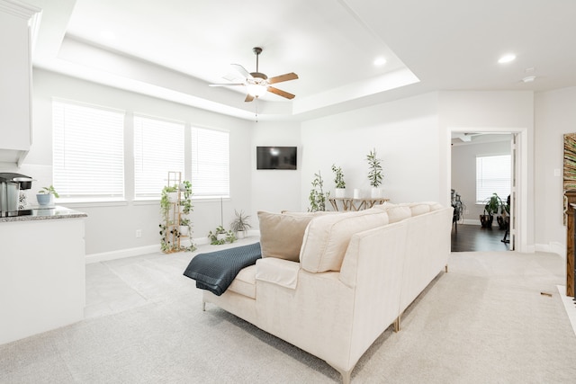 living room featuring light colored carpet, ceiling fan, and a tray ceiling