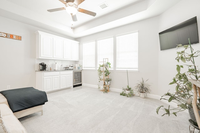 living area featuring light carpet, a tray ceiling, ceiling fan, and wine cooler