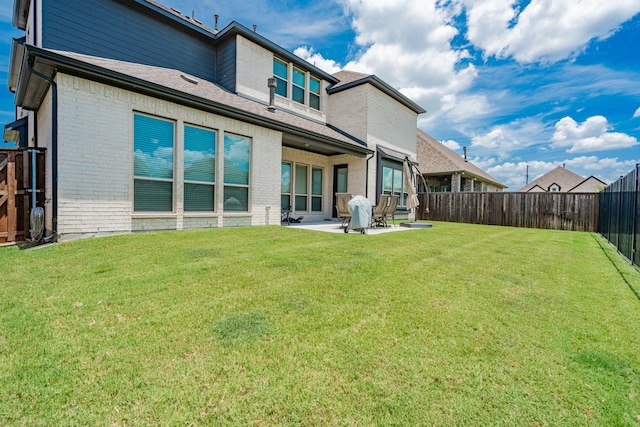 rear view of property featuring a yard, brick siding, a fenced backyard, and a patio area
