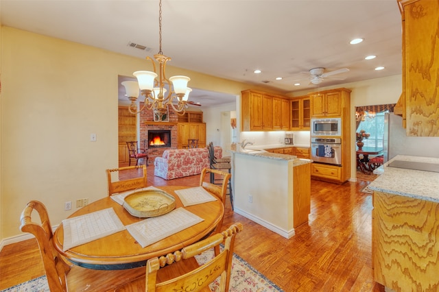 dining room featuring ceiling fan with notable chandelier, light hardwood / wood-style floors, a fireplace, and sink