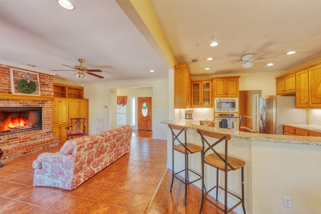 kitchen featuring light stone counters, kitchen peninsula, a fireplace, appliances with stainless steel finishes, and ceiling fan