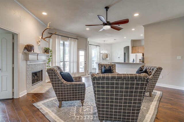 living room with dark wood-type flooring, ceiling fan with notable chandelier, a fireplace, and ornamental molding