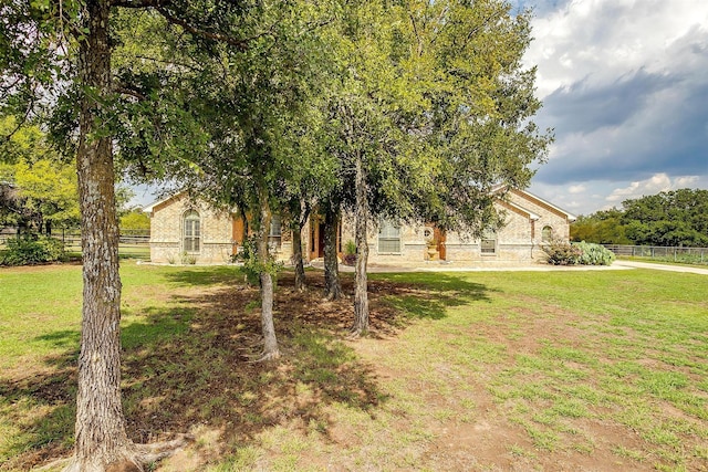 view of property hidden behind natural elements featuring a front yard and fence