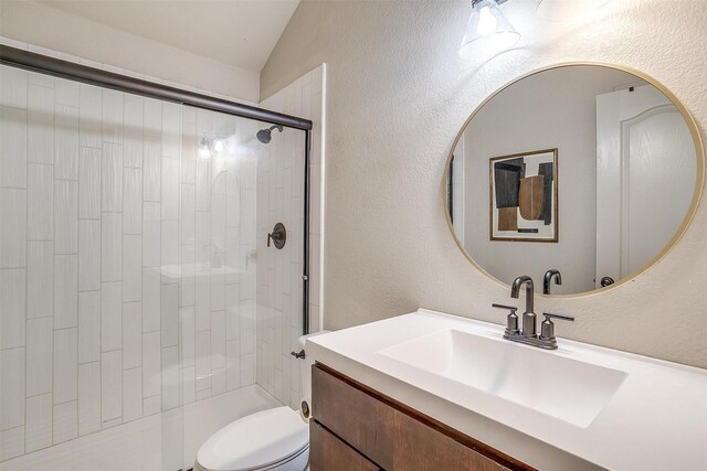 bathroom featuring vanity, toilet, a shower with shower door, and lofted ceiling