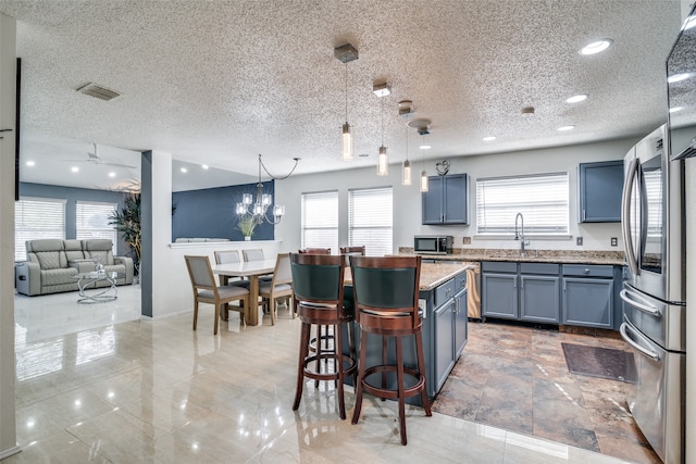 kitchen with stainless steel refrigerator, pendant lighting, a kitchen bar, blue cabinets, and a textured ceiling