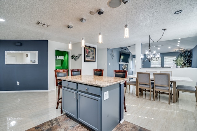 kitchen with a textured ceiling, a kitchen island, a notable chandelier, hanging light fixtures, and light stone counters