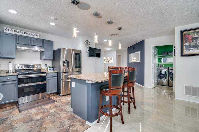 kitchen featuring a textured ceiling, washer and clothes dryer, a center island, stainless steel appliances, and hanging light fixtures