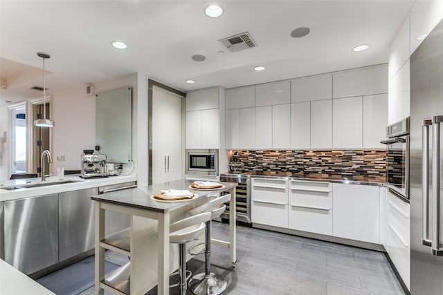 kitchen with pendant lighting, appliances with stainless steel finishes, tasteful backsplash, sink, and white cabinetry