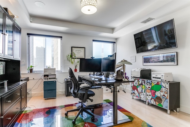 home office with a tray ceiling and light hardwood / wood-style floors