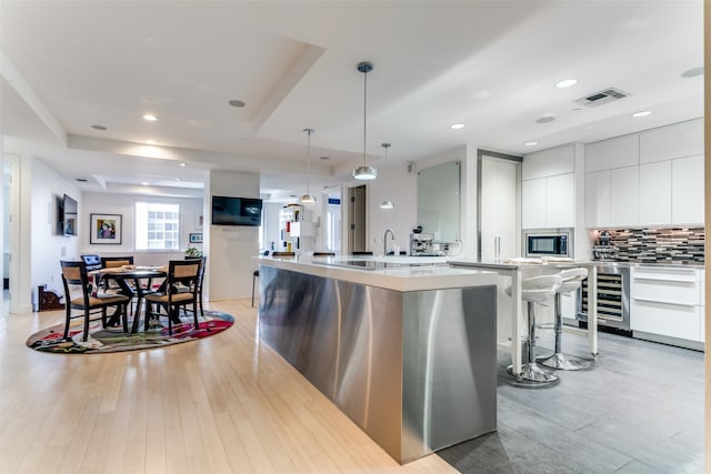 kitchen featuring light hardwood / wood-style flooring, beverage cooler, decorative backsplash, white cabinets, and a large island