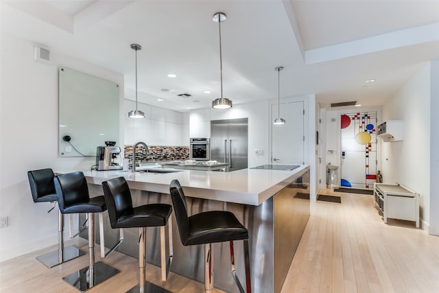 kitchen with light wood-type flooring, stainless steel appliances, sink, a kitchen breakfast bar, and pendant lighting