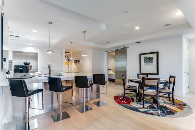 kitchen with light wood-type flooring, decorative light fixtures, white cabinetry, sink, and a breakfast bar area