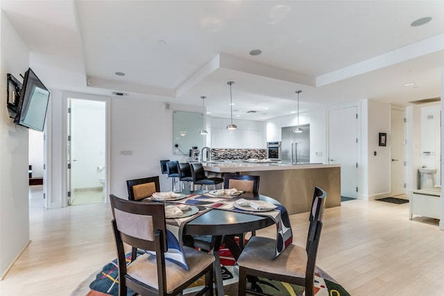 dining room with a raised ceiling and light hardwood / wood-style flooring