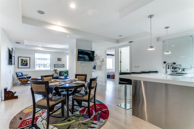 dining room featuring a large fireplace, a tray ceiling, sink, and light hardwood / wood-style flooring