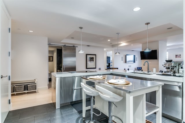 kitchen with a raised ceiling, decorative light fixtures, dark hardwood / wood-style flooring, a breakfast bar, and sink