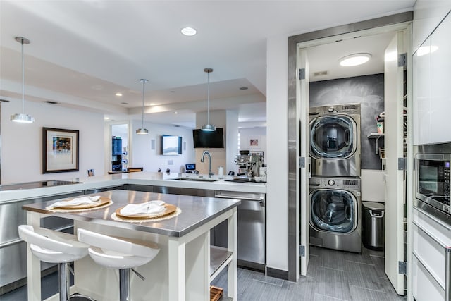 interior space featuring stainless steel counters, stacked washer / dryer, sink, hanging light fixtures, and white cabinets