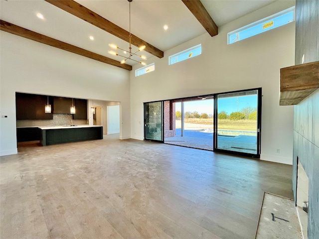 unfurnished living room with sink, a notable chandelier, beamed ceiling, a towering ceiling, and hardwood / wood-style floors