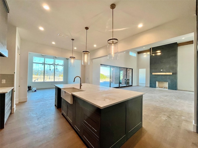 kitchen with a fireplace, sink, hanging light fixtures, light stone countertops, and a center island with sink