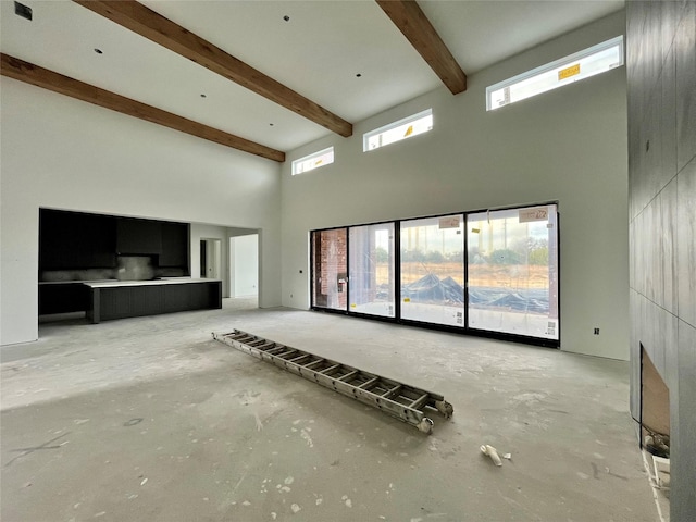 unfurnished living room with beam ceiling and a towering ceiling