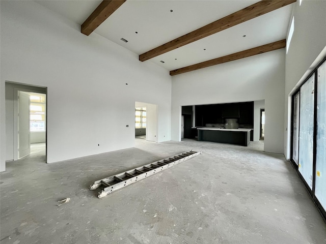 unfurnished living room with beam ceiling and a towering ceiling