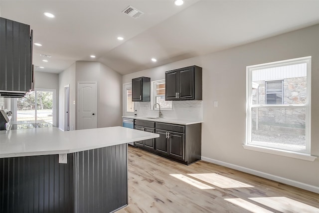 kitchen featuring backsplash, kitchen peninsula, light wood-type flooring, lofted ceiling, and sink