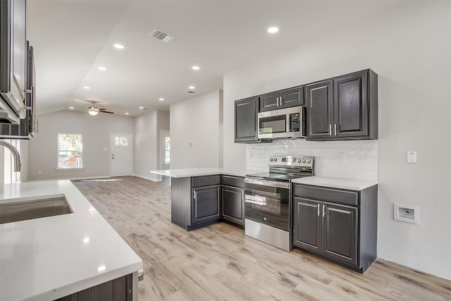 kitchen with appliances with stainless steel finishes, vaulted ceiling, ceiling fan, light hardwood / wood-style flooring, and sink