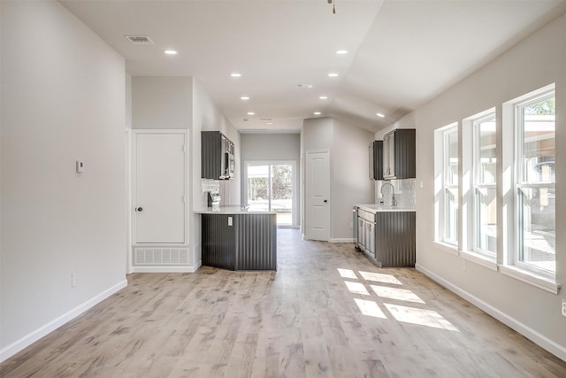 kitchen with light hardwood / wood-style floors, lofted ceiling, backsplash, and sink