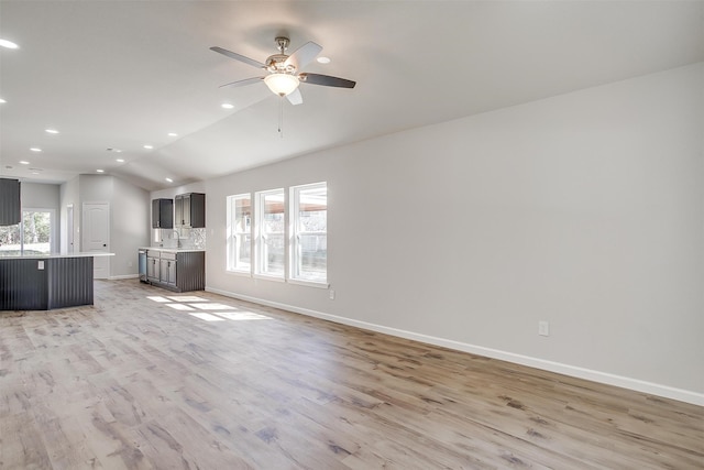 unfurnished living room featuring light hardwood / wood-style floors, vaulted ceiling, ceiling fan, and a wealth of natural light