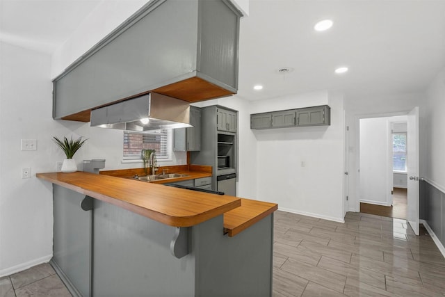 kitchen featuring exhaust hood, sink, a kitchen breakfast bar, kitchen peninsula, and gray cabinetry