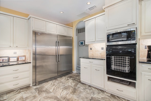 kitchen featuring decorative backsplash, white cabinetry, built in appliances, and dark stone counters