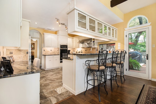 kitchen with dark stone countertops, white cabinetry, backsplash, kitchen peninsula, and wood-type flooring