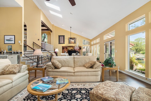 living room with dark hardwood / wood-style flooring, ceiling fan, a skylight, and high vaulted ceiling