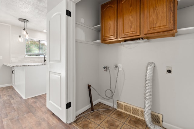 washroom with light hardwood / wood-style flooring, cabinets, a textured ceiling, and electric dryer hookup