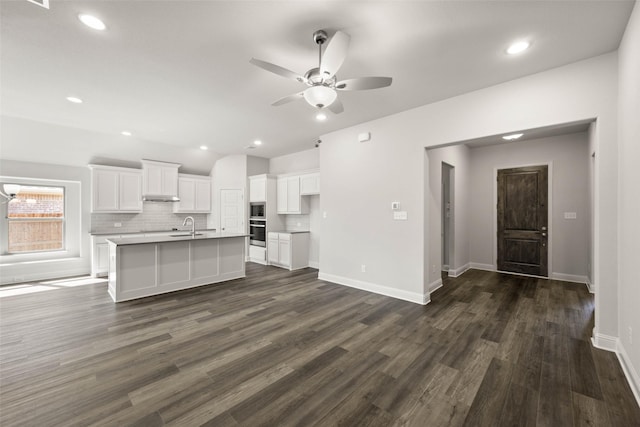 kitchen featuring an island with sink, dark wood-style flooring, a sink, and white cabinets