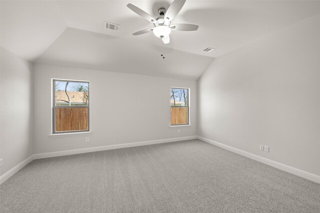 carpeted empty room with a wealth of natural light, visible vents, and vaulted ceiling