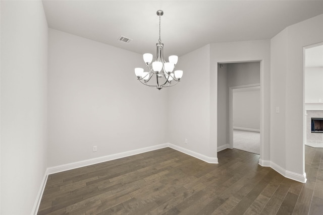 unfurnished dining area featuring visible vents, baseboards, dark wood-style floors, a fireplace, and a notable chandelier