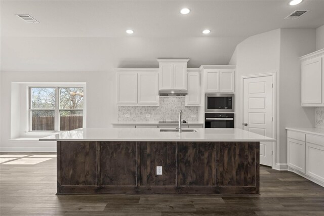 kitchen with under cabinet range hood, stainless steel microwave, visible vents, and a center island with sink