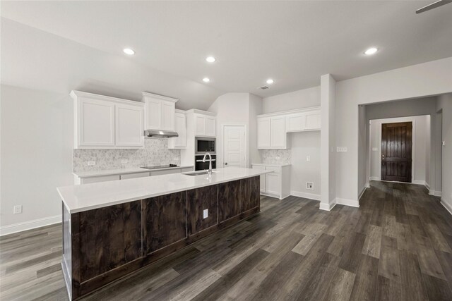 kitchen featuring a sink, a large island, under cabinet range hood, stainless steel microwave, and black electric cooktop